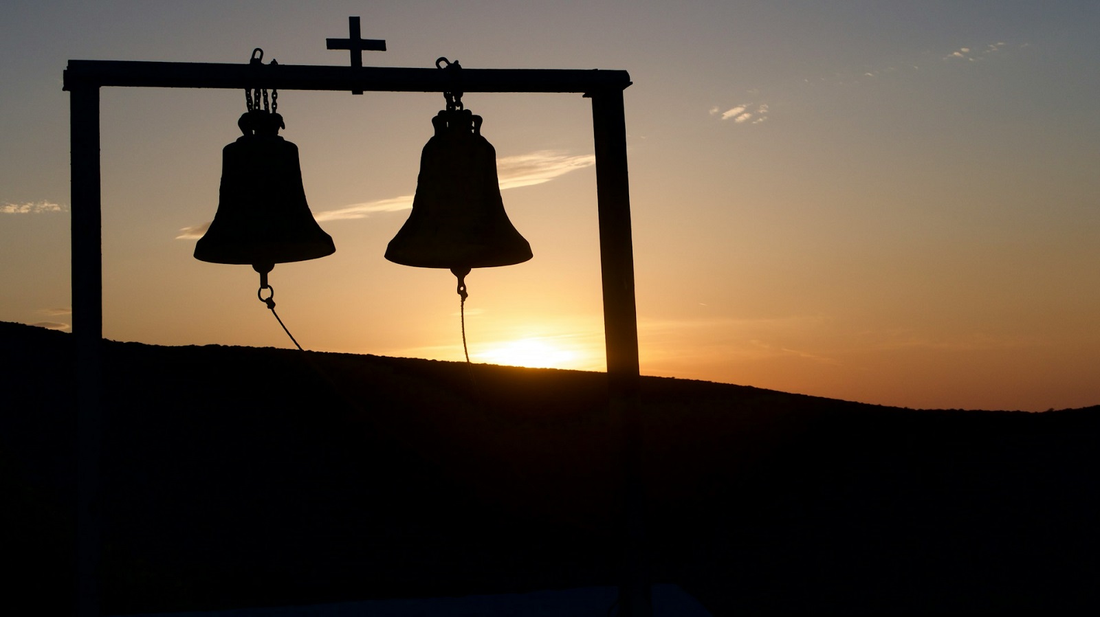 Due cambpane in ombra al tramonto con una croce sormontata nel mezzo